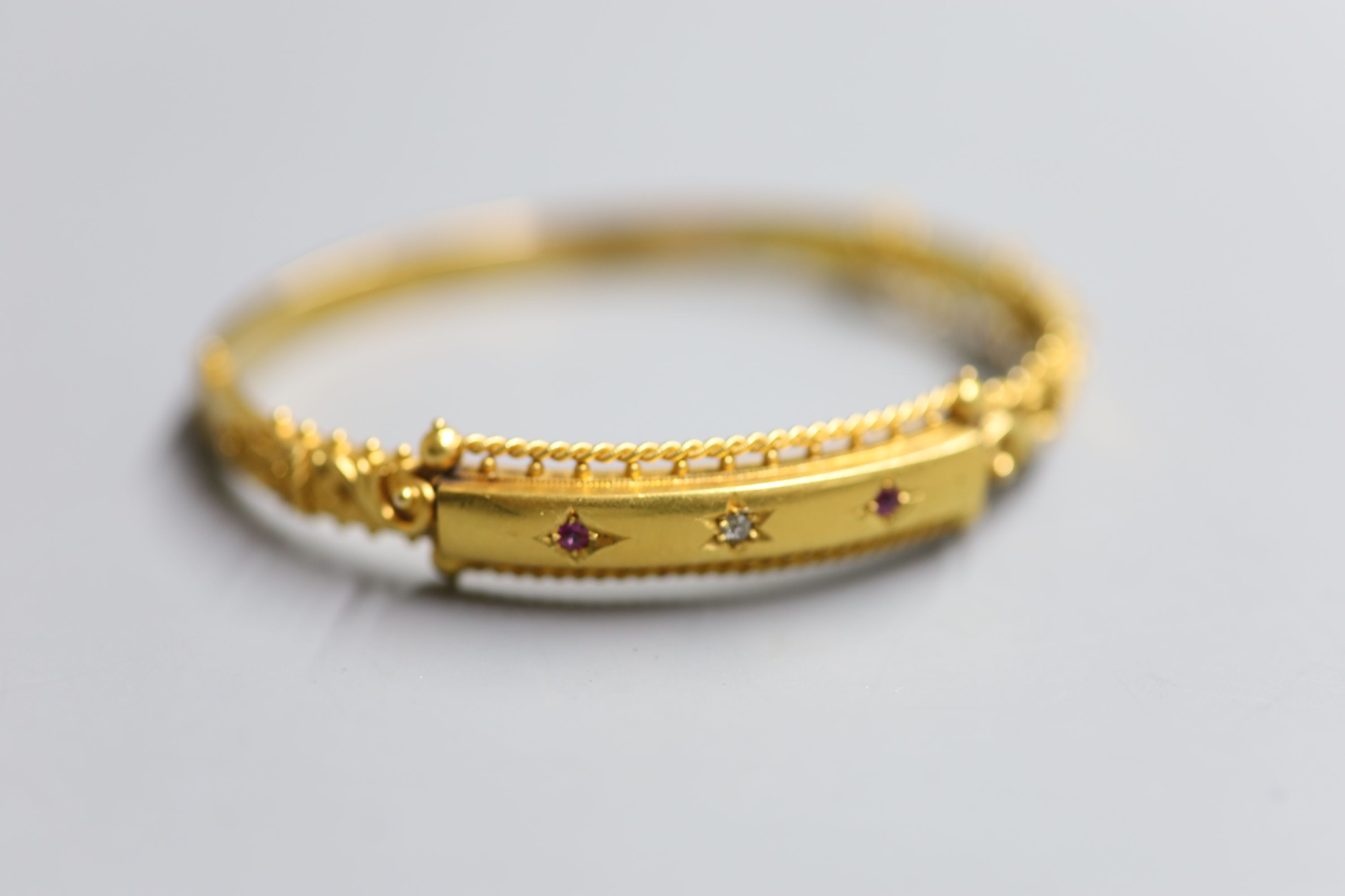 An Edwardian 15ct gold and gypsy set ruby and diamond three stone hinged bangle, gross 11.1 grams (a.f.).